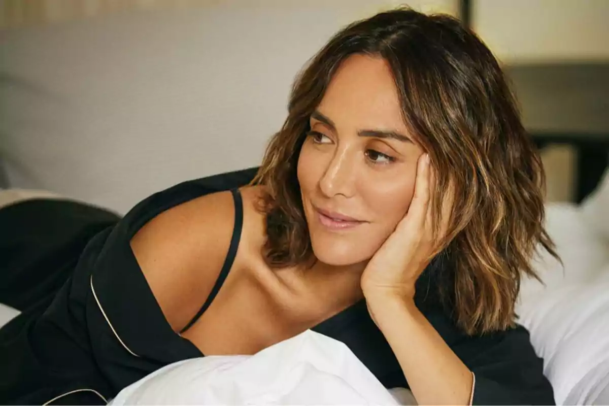 Una persona con cabello castaño y ondulado, recostada sobre una cama, mirando pensativamente hacia un lado. Una persona con cabello castaño y ondulado, recostada sobre una cama, mirando pensativamente hacia un lado.