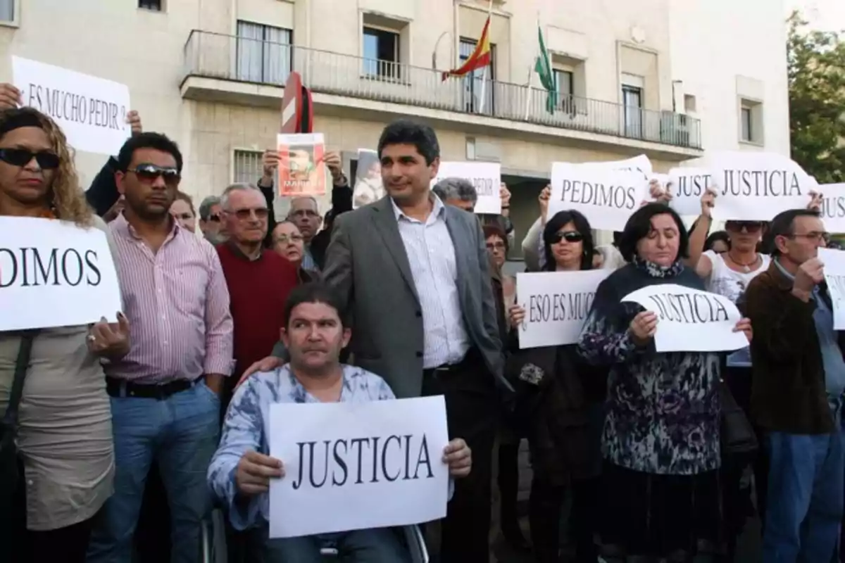 Un grupo de personas se manifiesta sosteniendo carteles que piden justicia frente a un edificio con banderas.