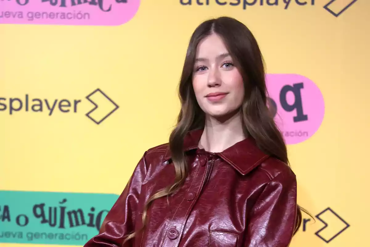 Una persona con chaqueta de cuero roja posando frente a un fondo amarillo con logotipos.