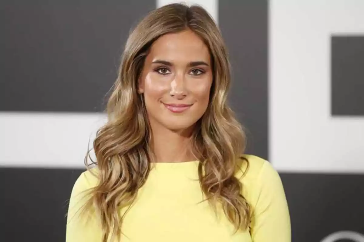 Mujer con cabello largo y ondulado, usando un vestido amarillo, sonriendo frente a un fondo desenfocado.