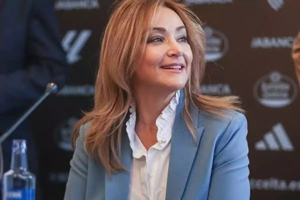 Una mujer sonriente con cabello castaño claro y vestida con un blazer azul y blusa blanca en un evento.