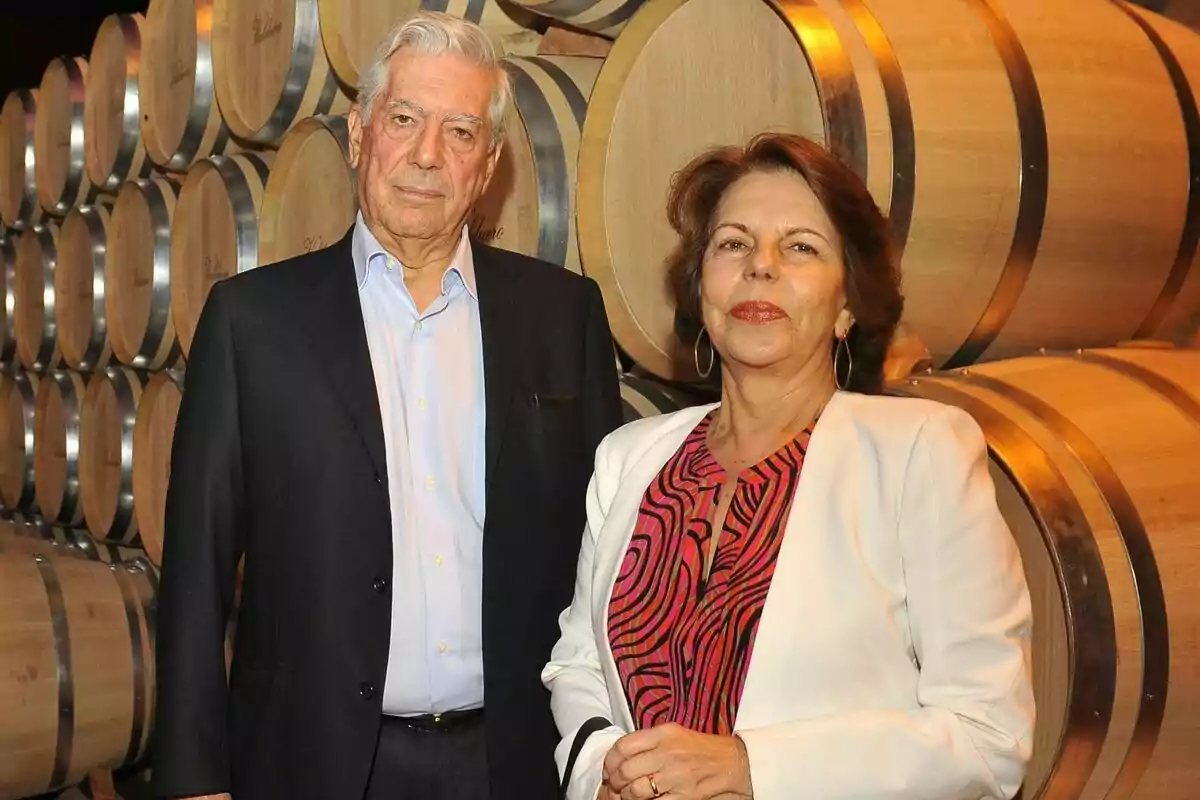 Mario Vargas Llosa y Patricia Llosa posando frente a barriles de madera en una bodega.