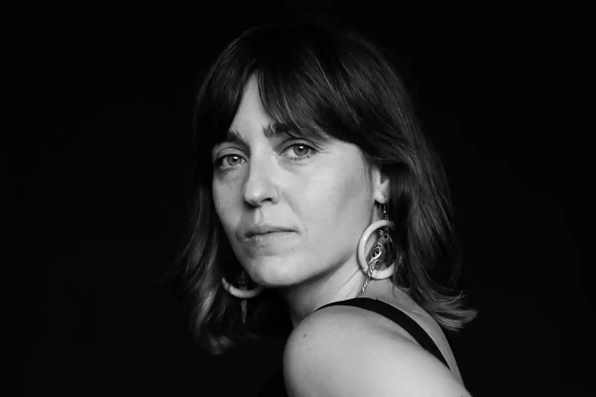 Retrato en blanco y negro de una mujer con cabello oscuro y aretes grandes mirando hacia la cámara.