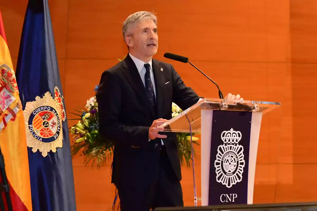 Un hombre de traje y corbata habla en un podio con el logotipo del Cuerpo Nacional de Policía, con una bandera de España y una bandera del Cuerpo Nacional de Policía a su lado.