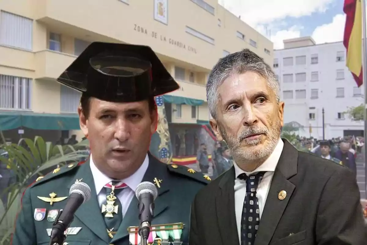 Dos hombres en uniforme y traje frente a un edificio de la Guardia Civil con una bandera española ondeando.