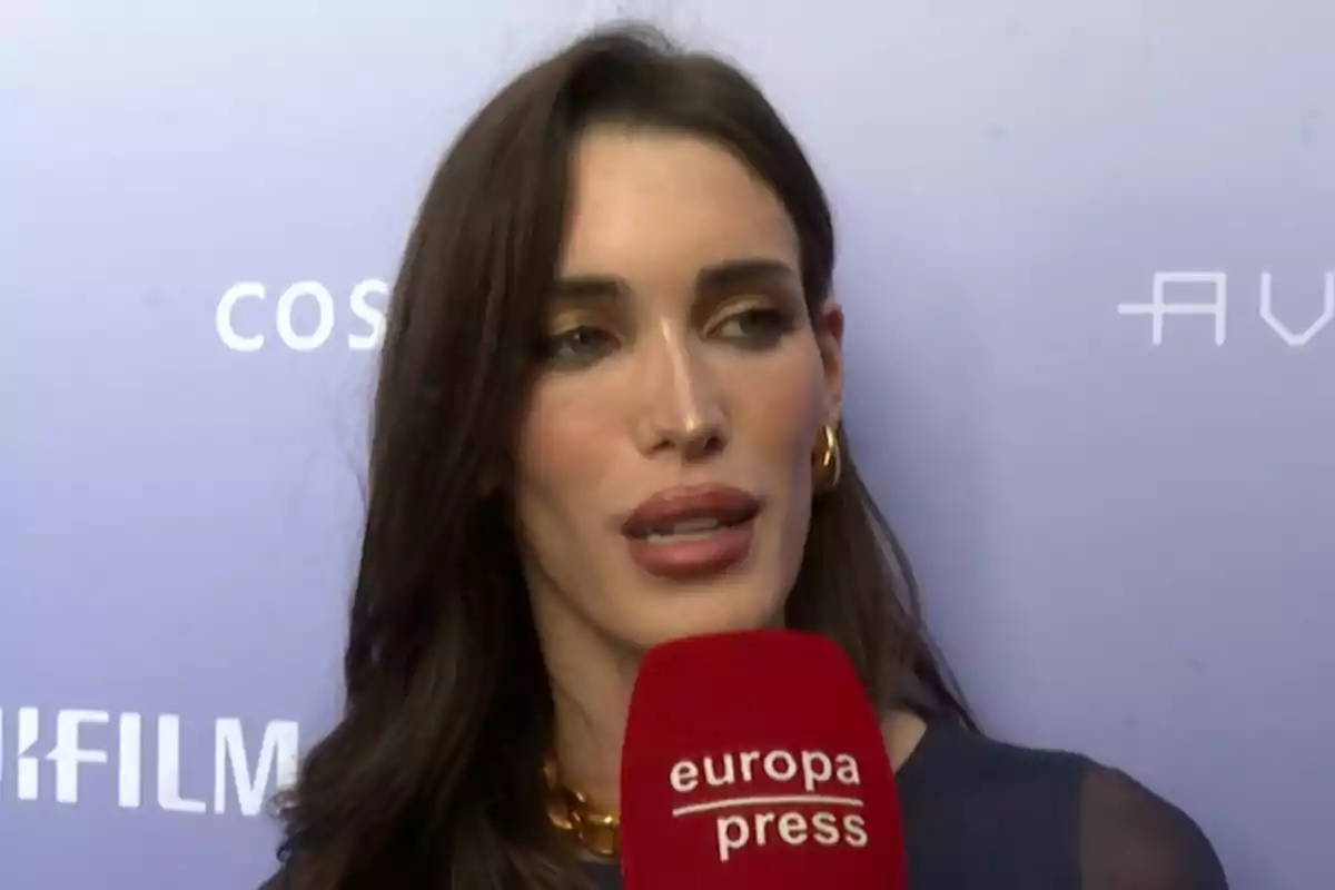 Marta López Álamo dando una entrevista con un micrófono rojo de europa press frente a un fondo lila con logotipos blancos Marta López Álamo dando una entrevista con un micrófono rojo de europa press frente a un fondo lila con logotipos blancos
