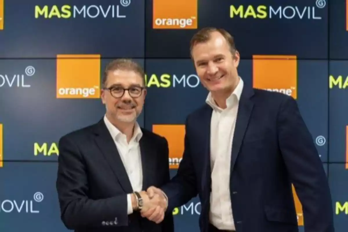 Dos hombres de traje se dan la mano frente a un fondo con logotipos de MASMOVIL y Orange.