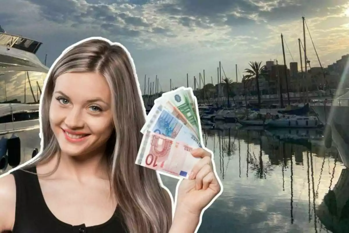 Una mujer sonriente sostiene billetes de euro frente a un puerto deportivo con yates y barcos al atardecer.