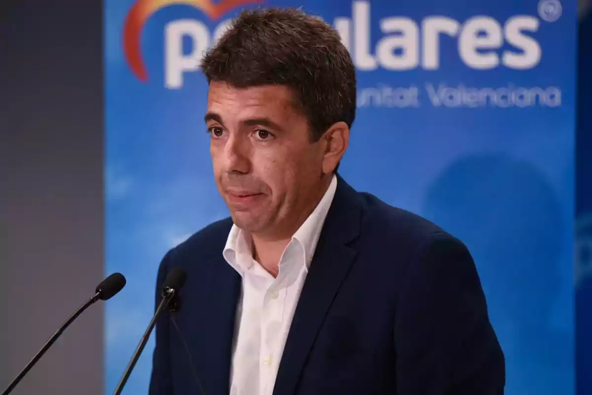 Hombre hablando en una conferencia de prensa con un fondo azul que muestra parte de un logotipo.