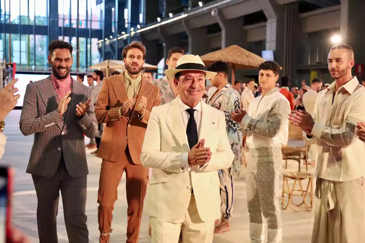 Un grupo de hombres elegantemente vestidos aplaude en un evento de moda en un espacio moderno y bien iluminado.