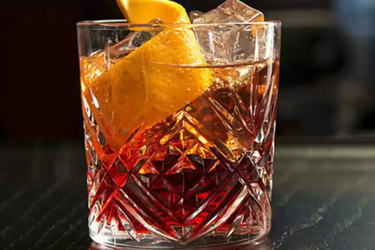 Vaso de cristal con bebida ámbar, hielo y una rodaja de naranja.
