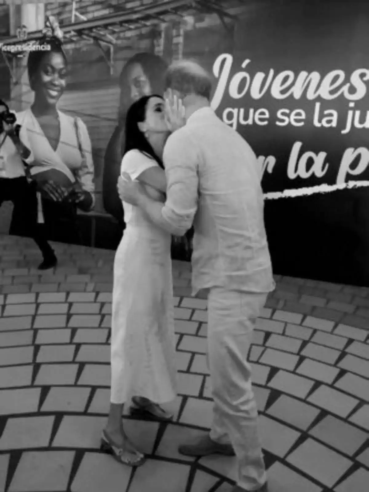 Meghan Markle y el príncipe Harry se abraza y se besa en la mejilla frente a un cartel que dice Meghan Markle y el príncipe Harry se abraza y se besa en la mejilla frente a un cartel que dice