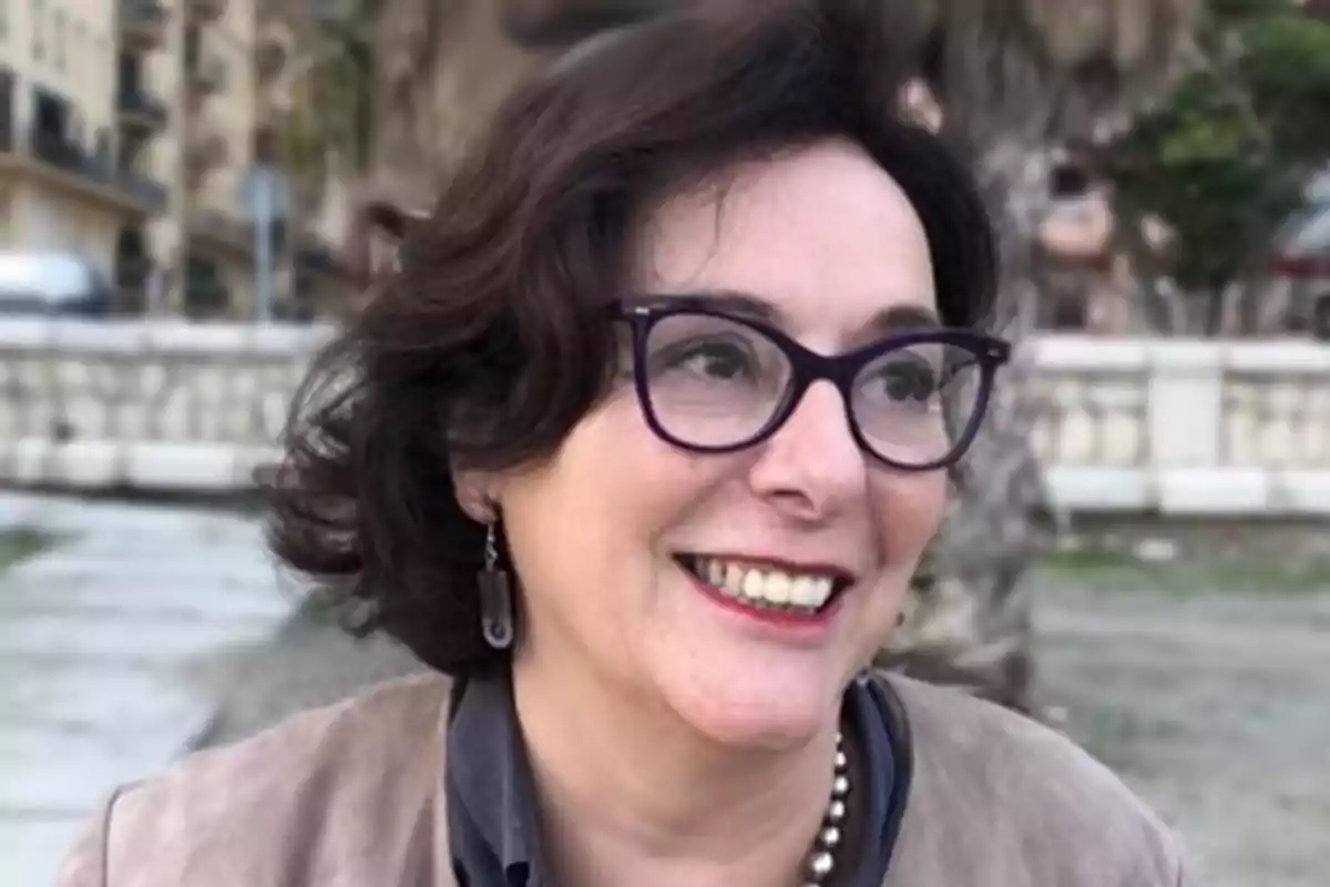 Una persona sonriente con gafas y cabello oscuro en un entorno al aire libre.