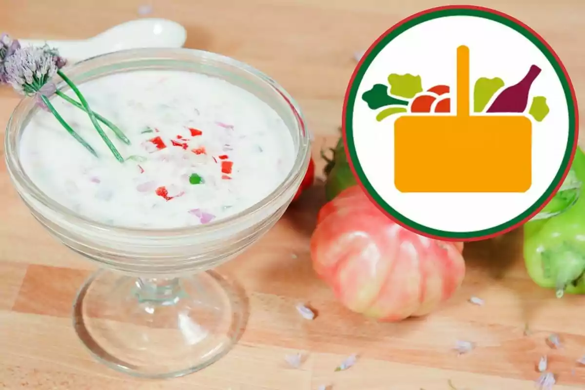 Un tazón de vidrio con una sopa blanca y trozos de vegetales, decorado con flores, junto a un logotipo de una canasta de vegetales. Un tazón de vidrio con una sopa blanca y trozos de vegetales, decorado con flores, junto a un logotipo de una canasta de vegetales.