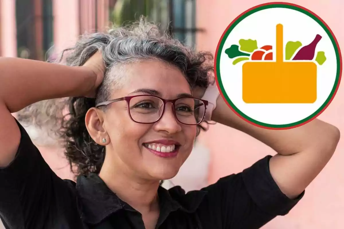 Mujer de cabello canoso y gafas sonríe mientras sostiene su cabeza con ambas manos, al fondo se observa un círculo con un dibujo de una canasta de alimentos Mujer de cabello canoso y gafas sonríe mientras sostiene su cabeza con ambas manos, al fondo se observa un círculo con un dibujo de una canasta de alimentos