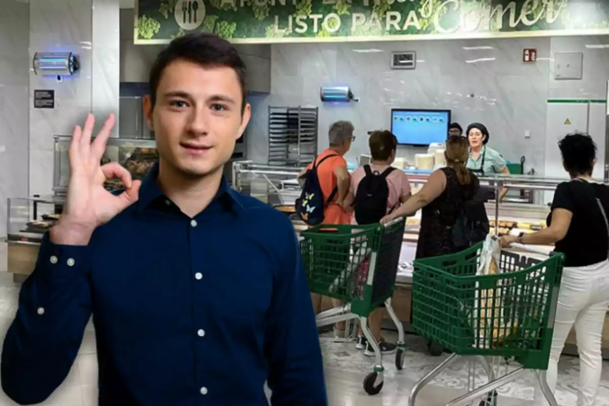 Un hombre con camisa azul hace un gesto de aprobación con la mano mientras en el fondo varias personas con carritos de supermercado esperan en un mostrador de comida.