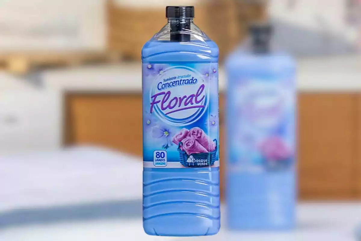 Botella de suavizante azul con etiqueta floral y toallas rosas en el centro de la imagen Botella de suavizante azul con etiqueta floral y toallas rosas en el centro de la imagen