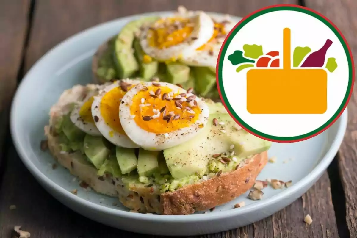 Tostada de aguacate con huevo cocido y semillas en un plato blanco junto a un icono de cesta de alimentos. Tostada de aguacate con huevo cocido y semillas en un plato blanco junto a un icono de cesta de alimentos.