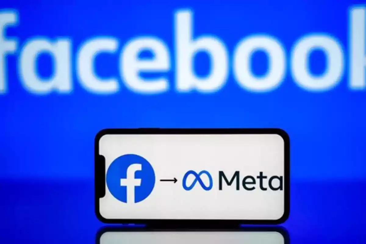 Teléfono mostrando el cambio de nombre de Facebook a Meta con el logo de Facebook al fondo. Teléfono mostrando el cambio de nombre de Facebook a Meta con el logo de Facebook al fondo.