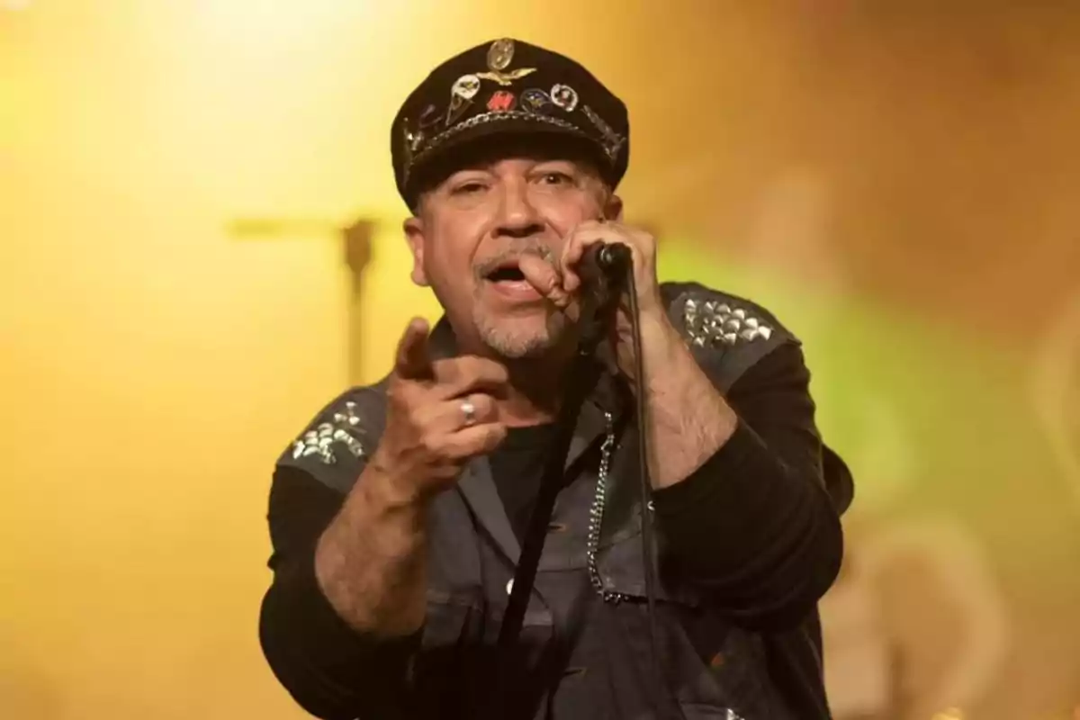 Un cantante con gorra y chaqueta decorada canta en un escenario iluminado.