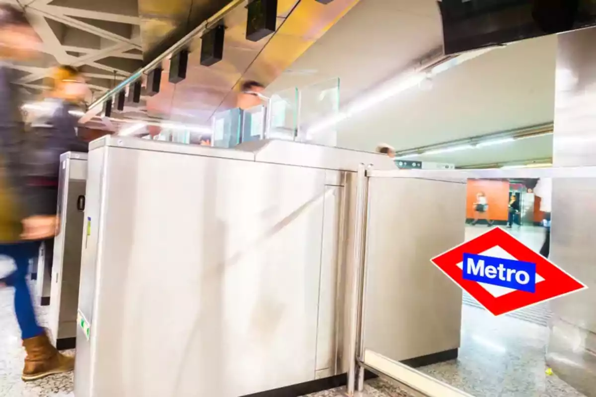 Personas pasando por los torniquetes de entrada en una estación de metro con el logotipo del Metro visible en primer plano Personas pasando por los torniquetes de entrada en una estación de metro con el logotipo del Metro visible en primer plano