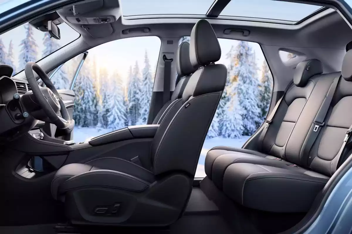 Interior de un MG ZS EV con asientos de cuero negro y techo panorámico, con un paisaje nevado visible a través de las ventanas.