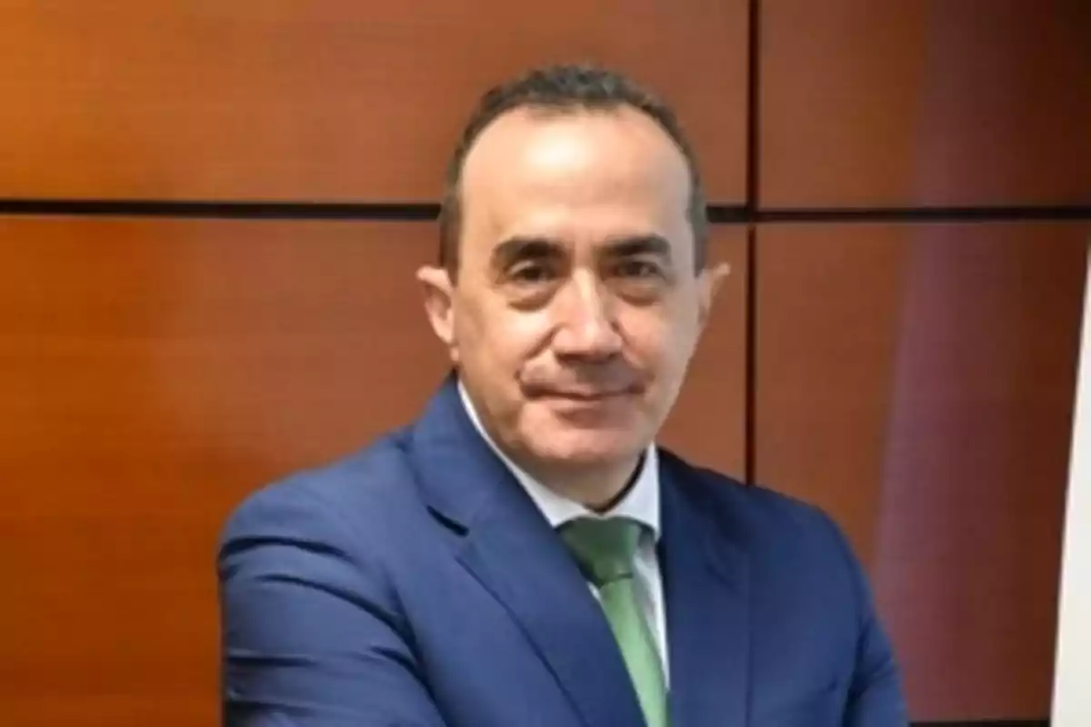 Un hombre con traje azul y corbata verde posando frente a un fondo de madera. Un hombre con traje azul y corbata verde posando frente a un fondo de madera.
