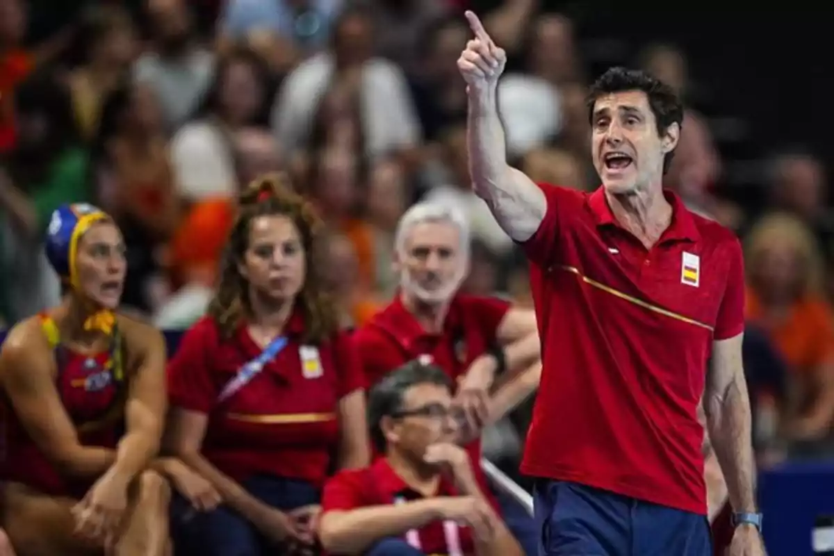 Un entrenador de waterpolo da instrucciones enérgicamente mientras el equipo observa desde el banquillo.