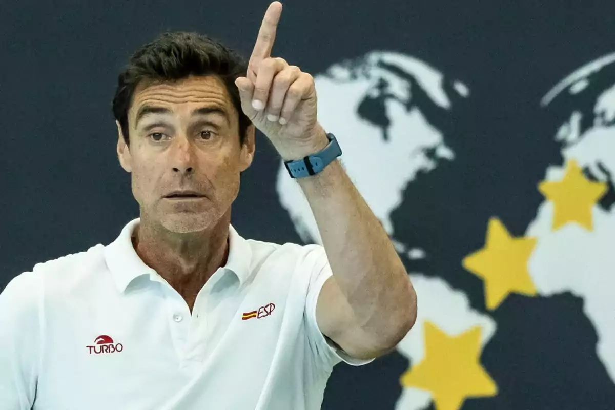 Un hombre con camiseta blanca señala hacia arriba con el dedo índice frente a un fondo de mapa y estrellas amarillas.