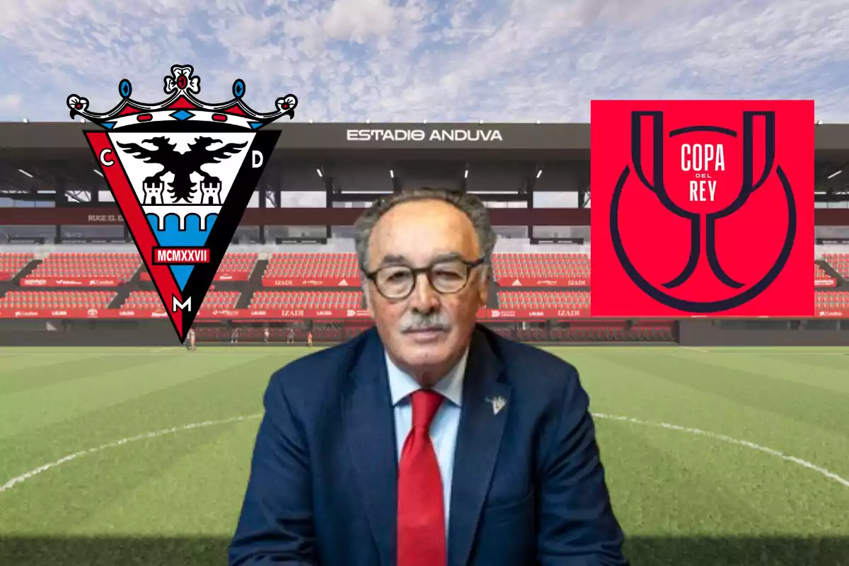 Hombre con gafas y traje azul sentado en un estadio de fútbol con el escudo del CD Mirandés a la izquierda y el logo de la Copa del Rey a la derecha Hombre con gafas y traje azul sentado en un estadio de fútbol con el escudo del CD Mirandés a la izquierda y el logo de la Copa del Rey a la derecha