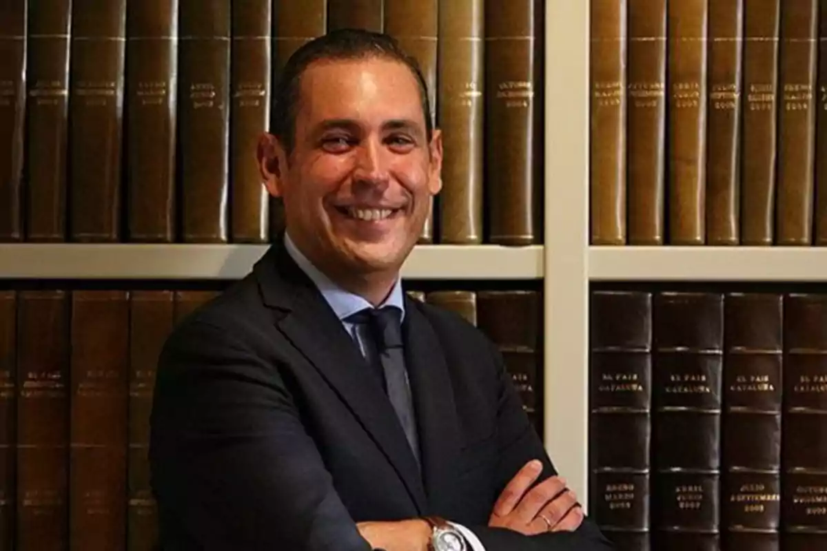 Hombre de traje sonriendo con los brazos cruzados frente a una estantería llena de libros antiguos Hombre de traje sonriendo con los brazos cruzados frente a una estantería llena de libros antiguos