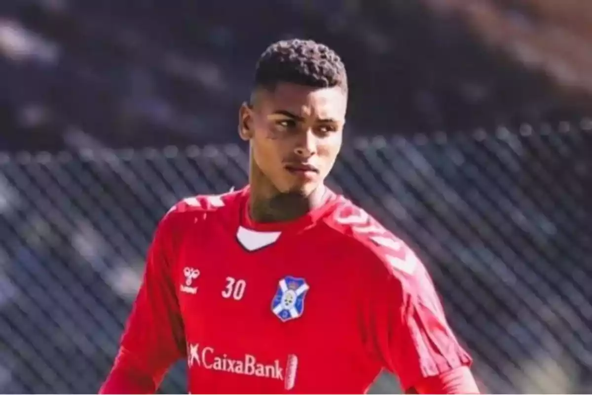 Jugador de fútbol con camiseta roja del equipo CD Tenerife en un campo de entrenamiento.