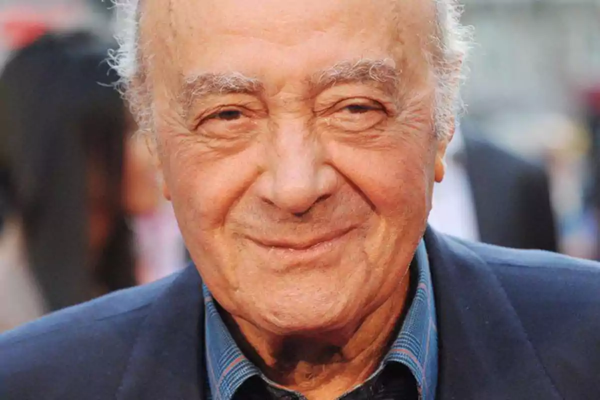 Mohamed Al-Fayed con cabello canoso y expresión sonriente, vestido con una camisa azul y una chaqueta oscura.