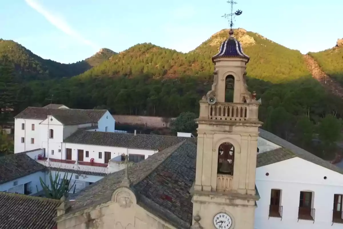 Vista aérea de un edificio histórico con campanario y reloj rodeado de montañas y vegetación.