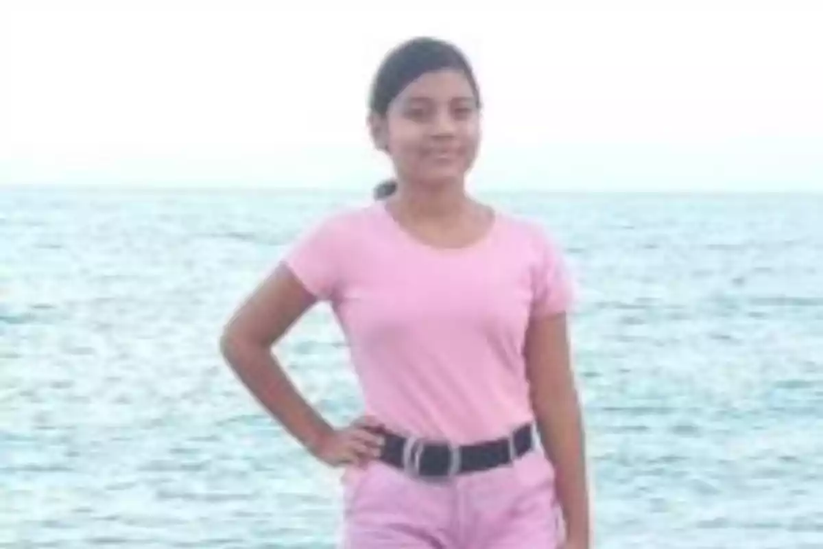 Una joven con camiseta rosa y pantalones cortos rosados posando frente al mar.