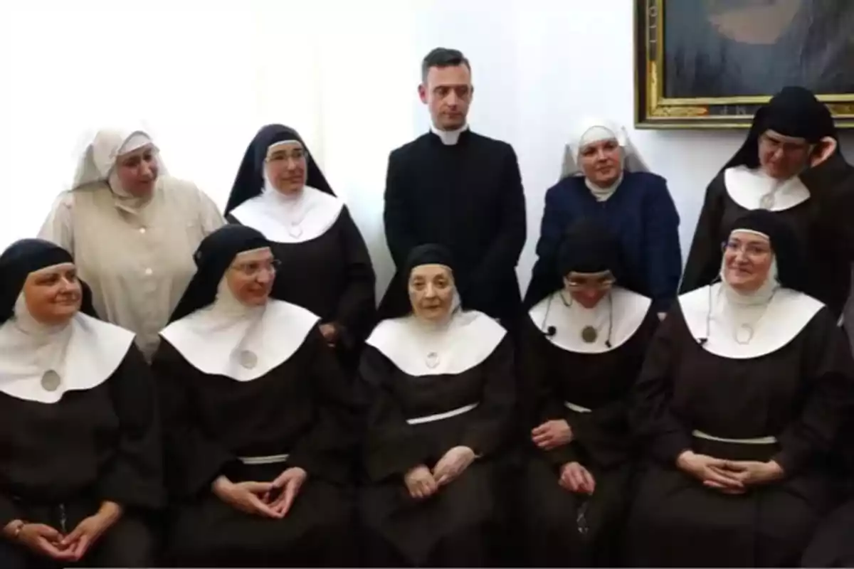 Un grupo de monjas y un sacerdote posan para una foto en una habitación iluminada.