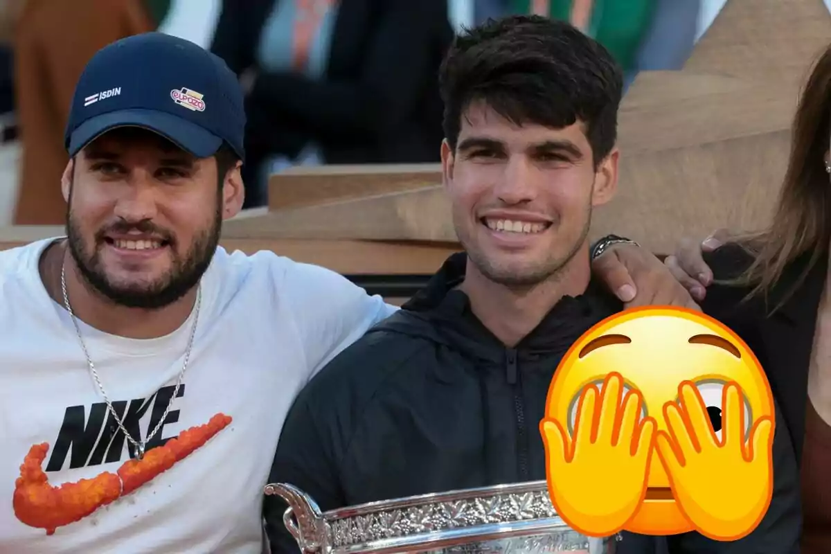 Álvaro Alcaraz y Carlos Alcaraz sonrientes posan juntos, Álvaro lleva una gorra y una camiseta blanca con el logo de Nike, mientras que Carlos sostiene un trofeo y tiene un emoji cubriendo parte de su rostro.