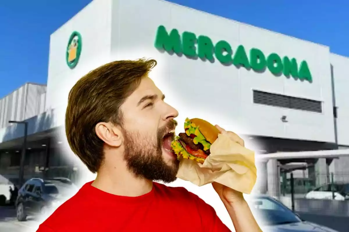 Un hombre con barba y camiseta roja está a punto de morder una hamburguesa frente a un edificio con el letrero de "Mercadona".