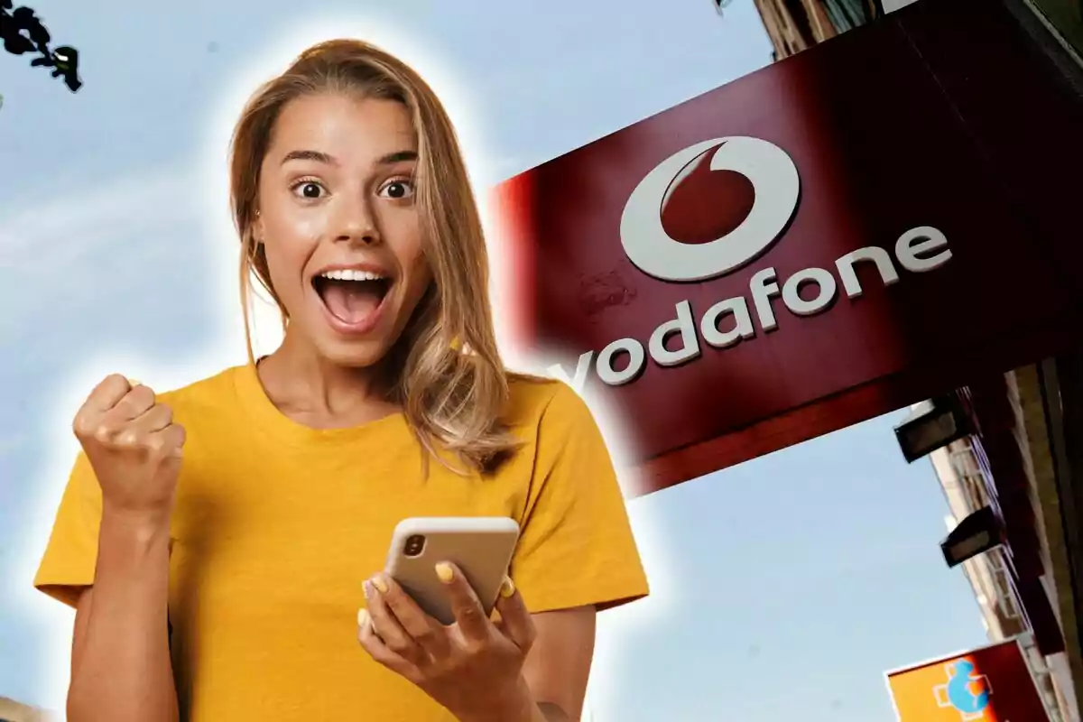 Mujer emocionada con camiseta amarilla sosteniendo un teléfono móvil frente a un cartel de Vodafone.