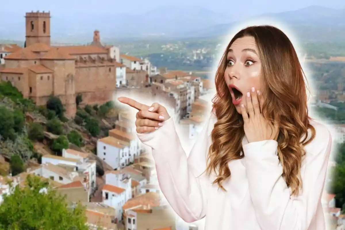 Una mujer con expresión de sorpresa y señalando con el dedo, con un fondo de un pueblo con casas blancas y una iglesia de piedra.