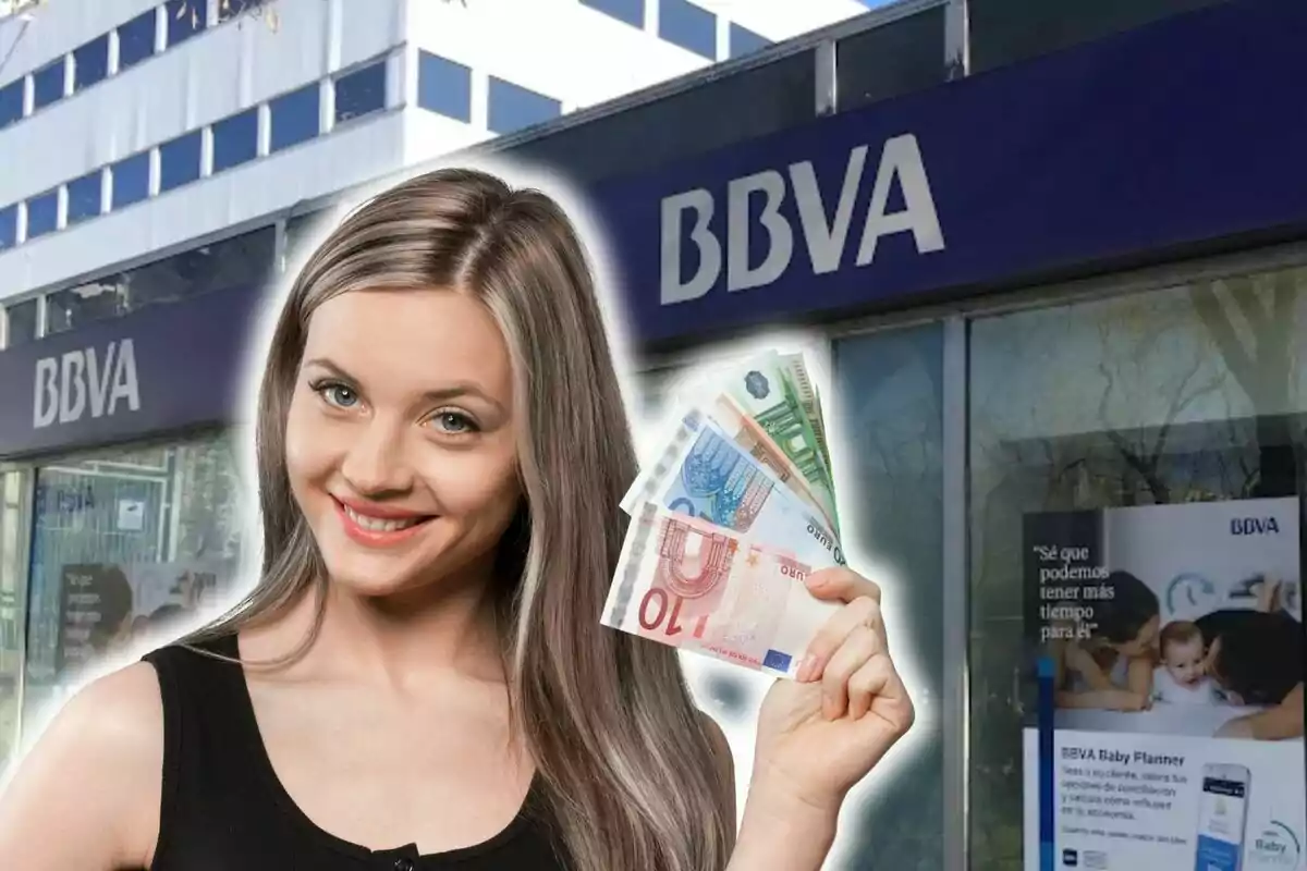 Una mujer sonriente sostiene billetes de euro frente a una sucursal del banco BBVA.