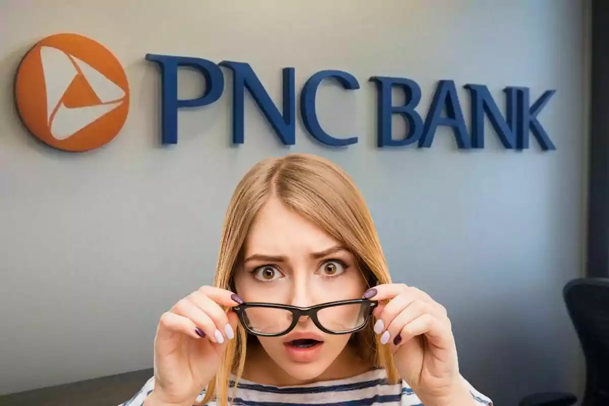 A person with a surprised expression holds their glasses in front of a PNC Bank sign. A person with a surprised expression holds their glasses in front of a PNC Bank sign.