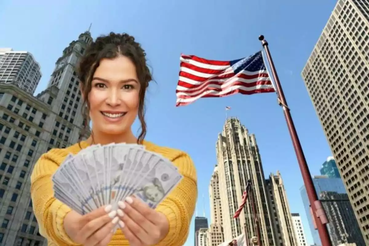 Mujer sonriente sostiene billetes de dólares frente a edificios altos y una bandera de Estados Unidos en un día soleado