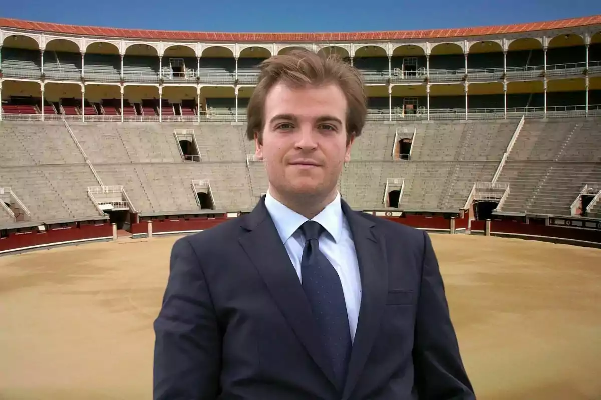 Un hombre con traje y corbata está de pie en el centro de una plaza de toros vacía.