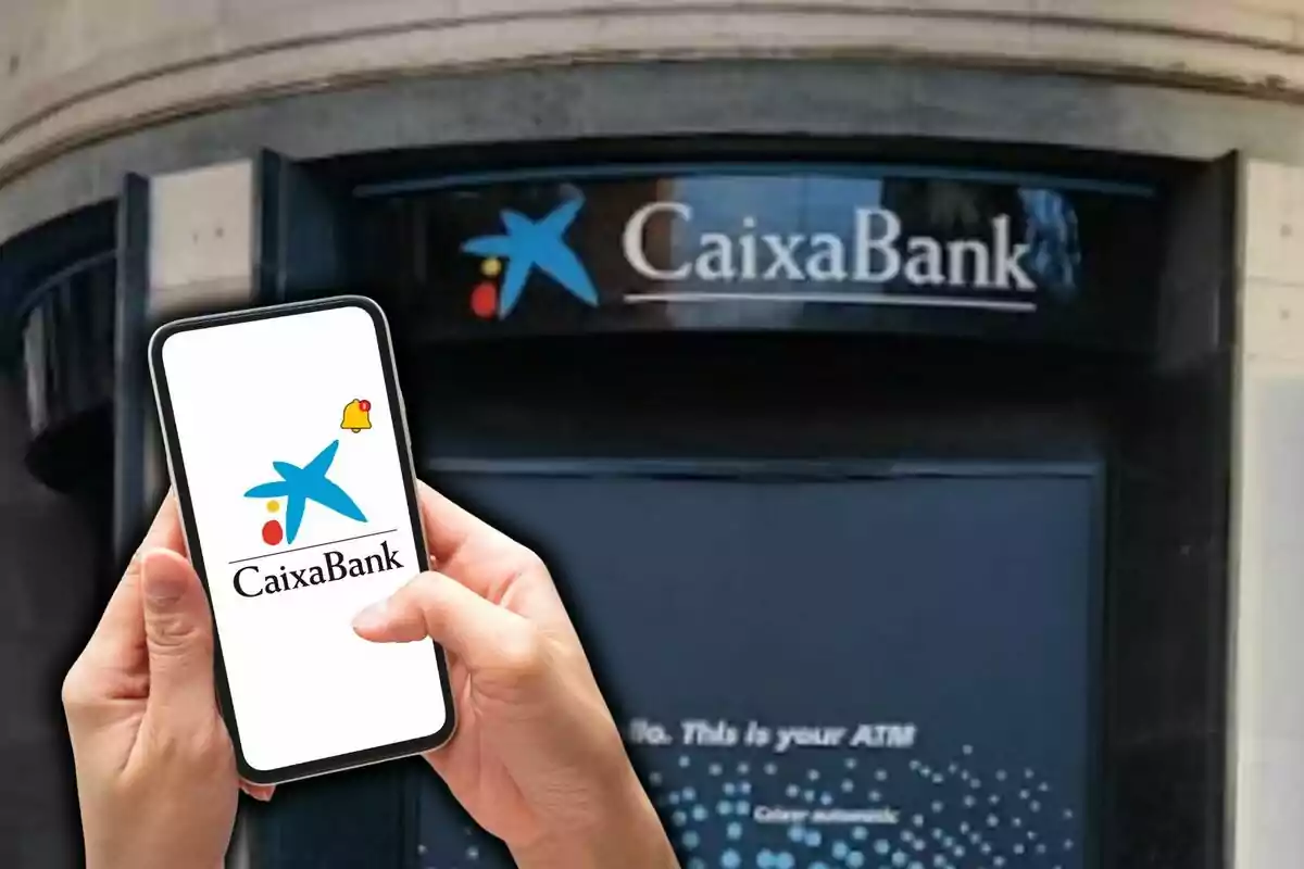 Una persona sostiene un teléfono móvil que muestra el logo de CaixaBank frente a una sucursal del banco.