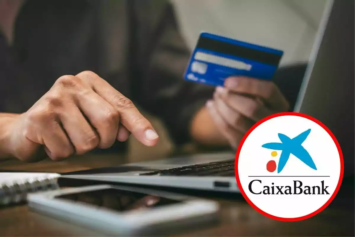 Persona usando una tarjeta de crédito frente a una computadora portátil con el logo de CaixaBank en primer plano.