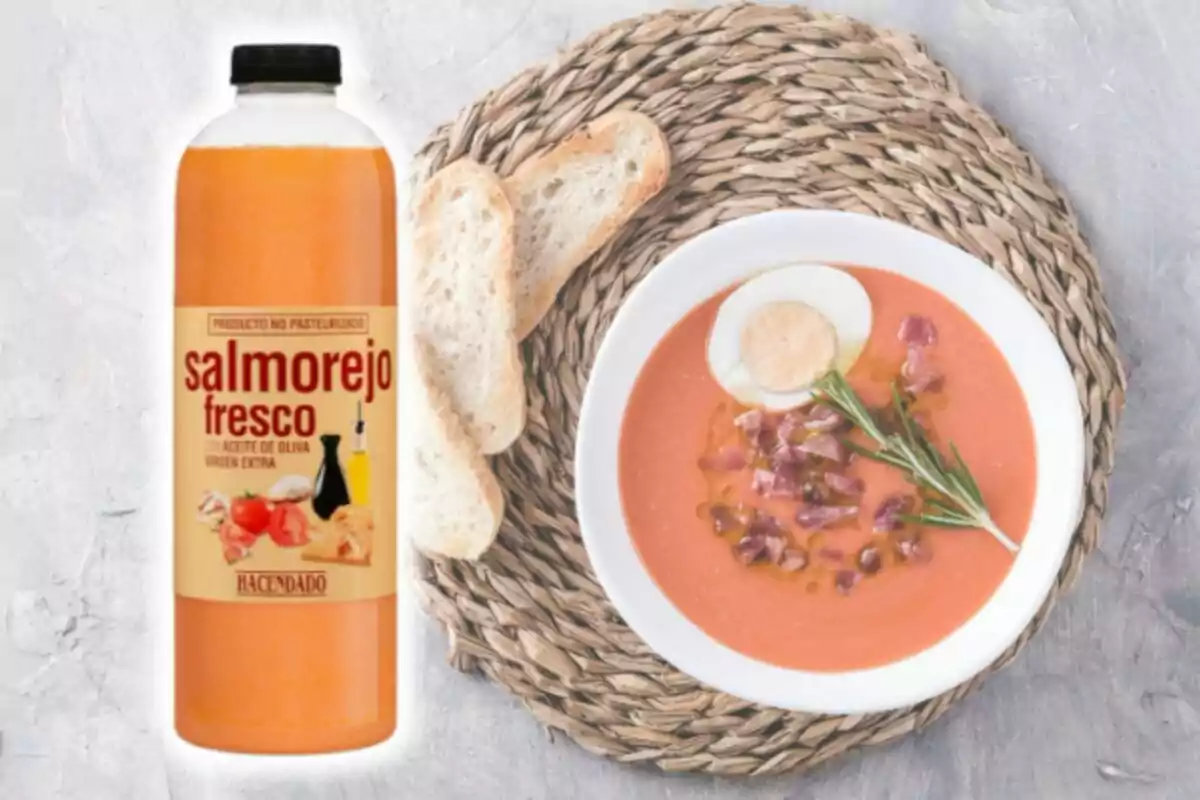 Una botella de salmorejo fresco junto a un plato servido con huevo cocido, jamón y pan sobre un mantel de mimbre. Una botella de salmorejo fresco junto a un plato servido con huevo cocido, jamón y pan sobre un mantel de mimbre.