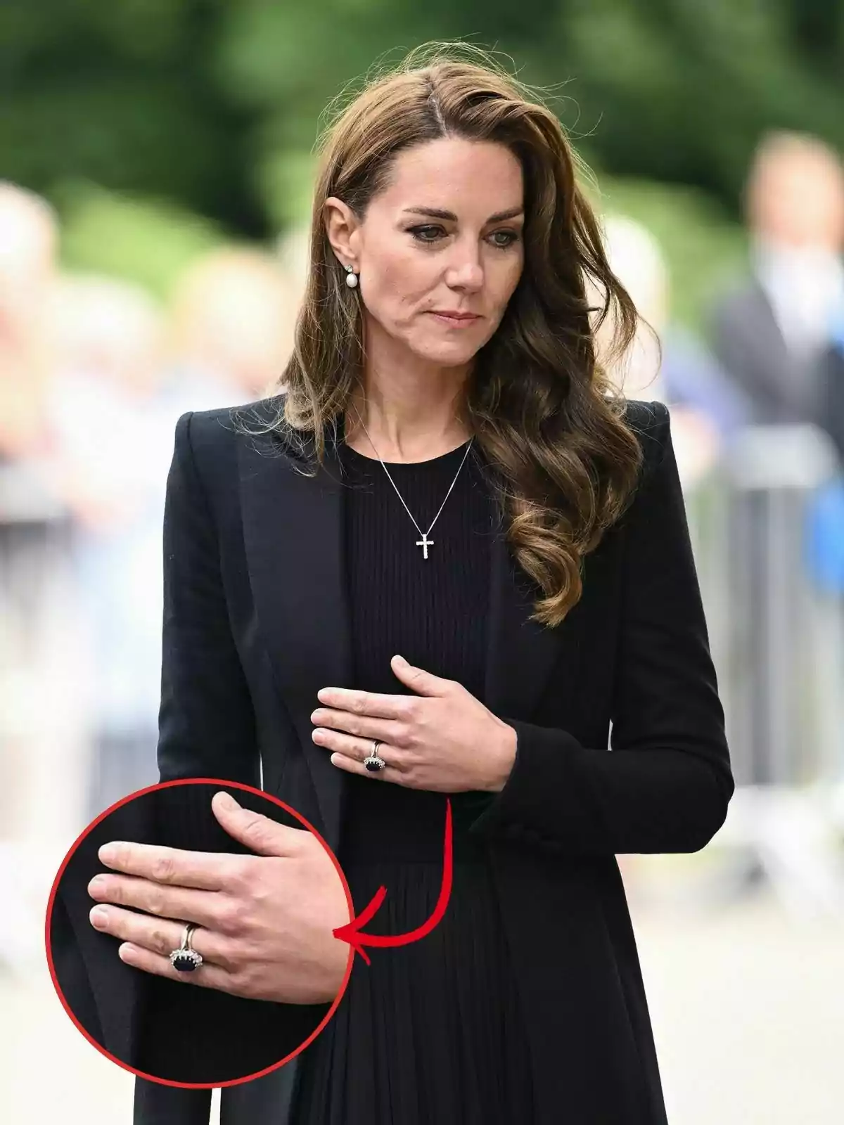 Kate Middleton con cabello castaño y vestido negro, con una mano sobre el pecho mostrando un anillo destacado en un círculo.