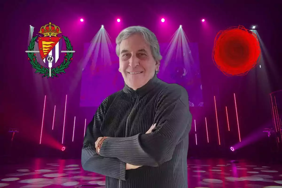 Un hombre de cabello canoso y suéter oscuro sonríe con los brazos cruzados en un escenario iluminado con luces moradas y símbolos en el fondo.