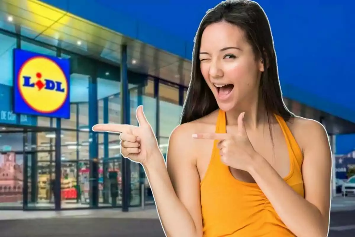 Una mujer sonriente con camiseta naranja hace un gesto de pistola con las manos frente a la entrada de una tienda Lidl.